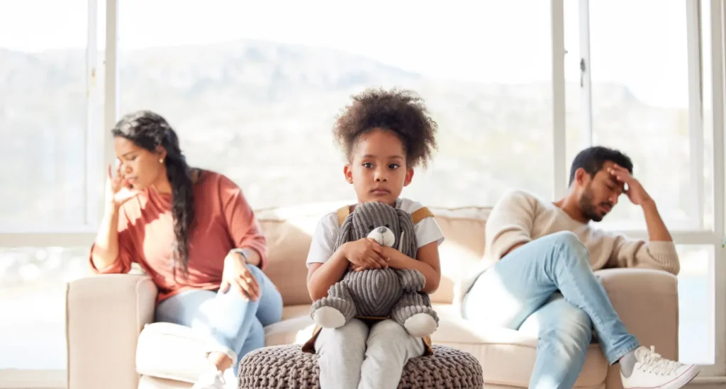 Sad young daughter holding her stuffed animal while sitting in between parents who are facing away from each other